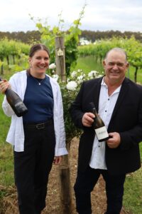 the owners of the pemerbley winery in Pemberton, holding a pinot noir and chardonnay wine bottle.