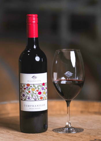 millbrook tempranillo wine bottle with a glass on an oak barrel.